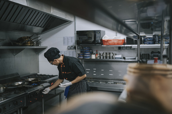 Chef working under a commercial kitchen canopy with grease filters visible