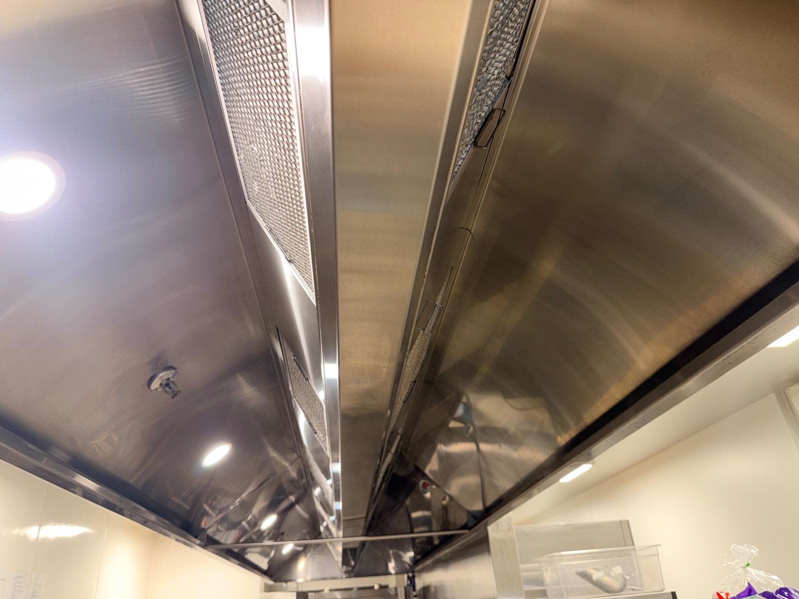 Clean stainless steel commercial kitchen canopy underside with filters in place, viewed from below